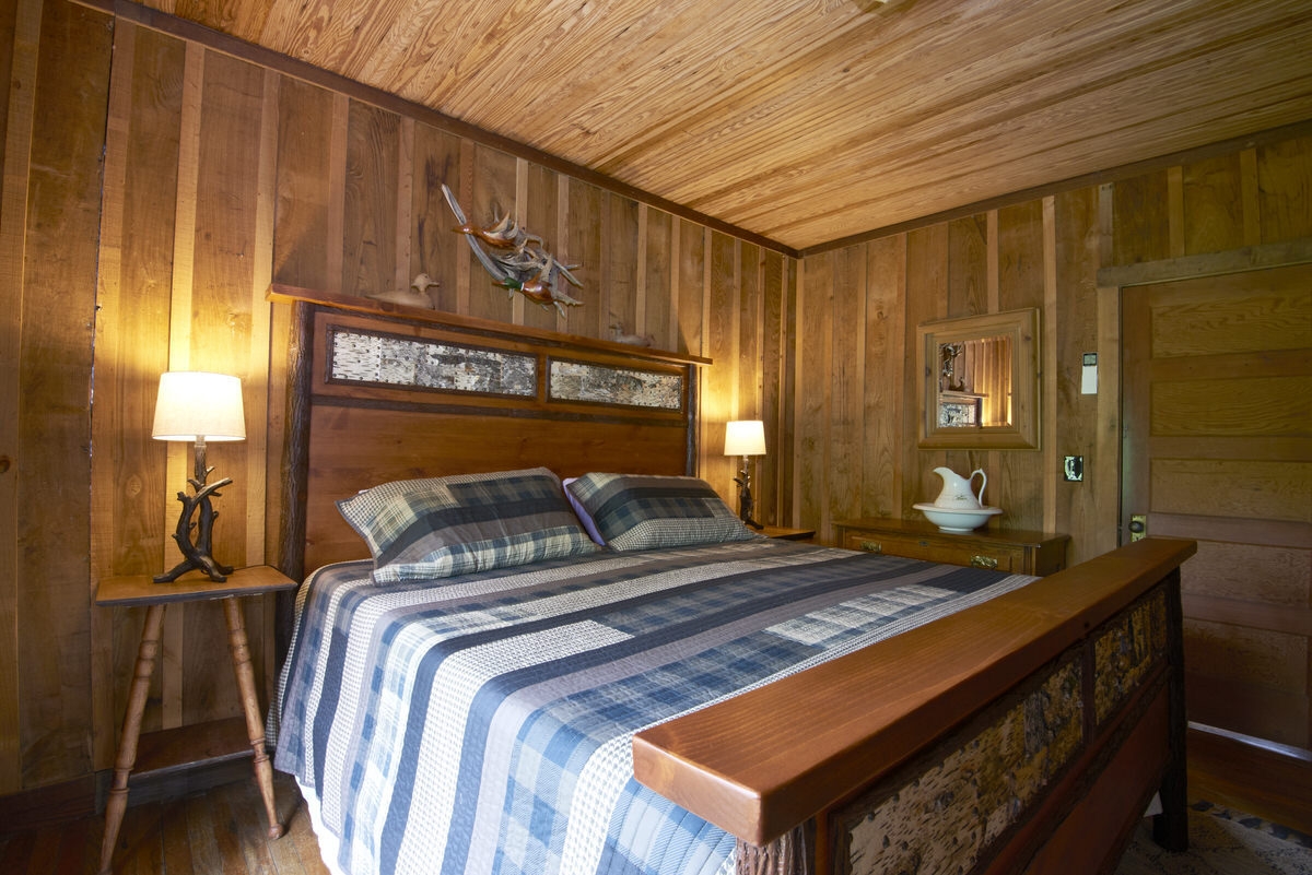 Rustic bedroom with a wooden bed frame, blue striped bedding, and wooden walls.
