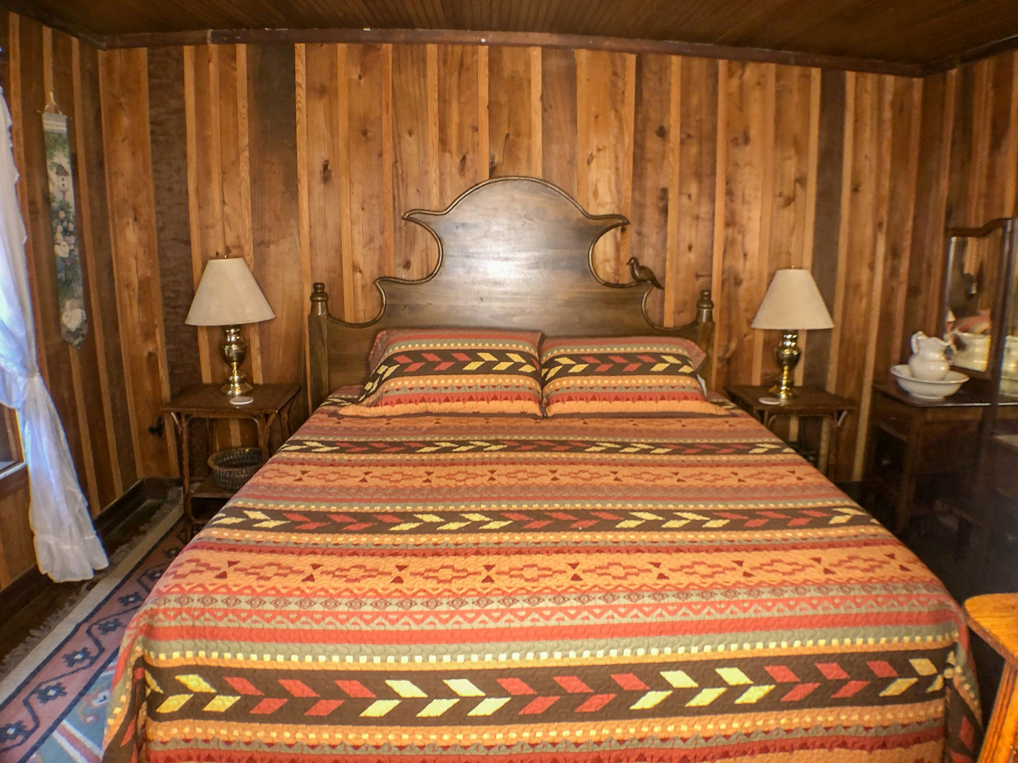 Rustic bedroom with a wooden headboard, colorful patterned bedspread, and wooden walls.