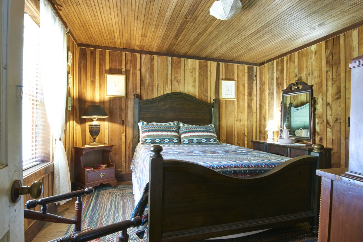 Rustic bedroom with a dark wooden bed frame, patterned bedspread, and wooden walls.