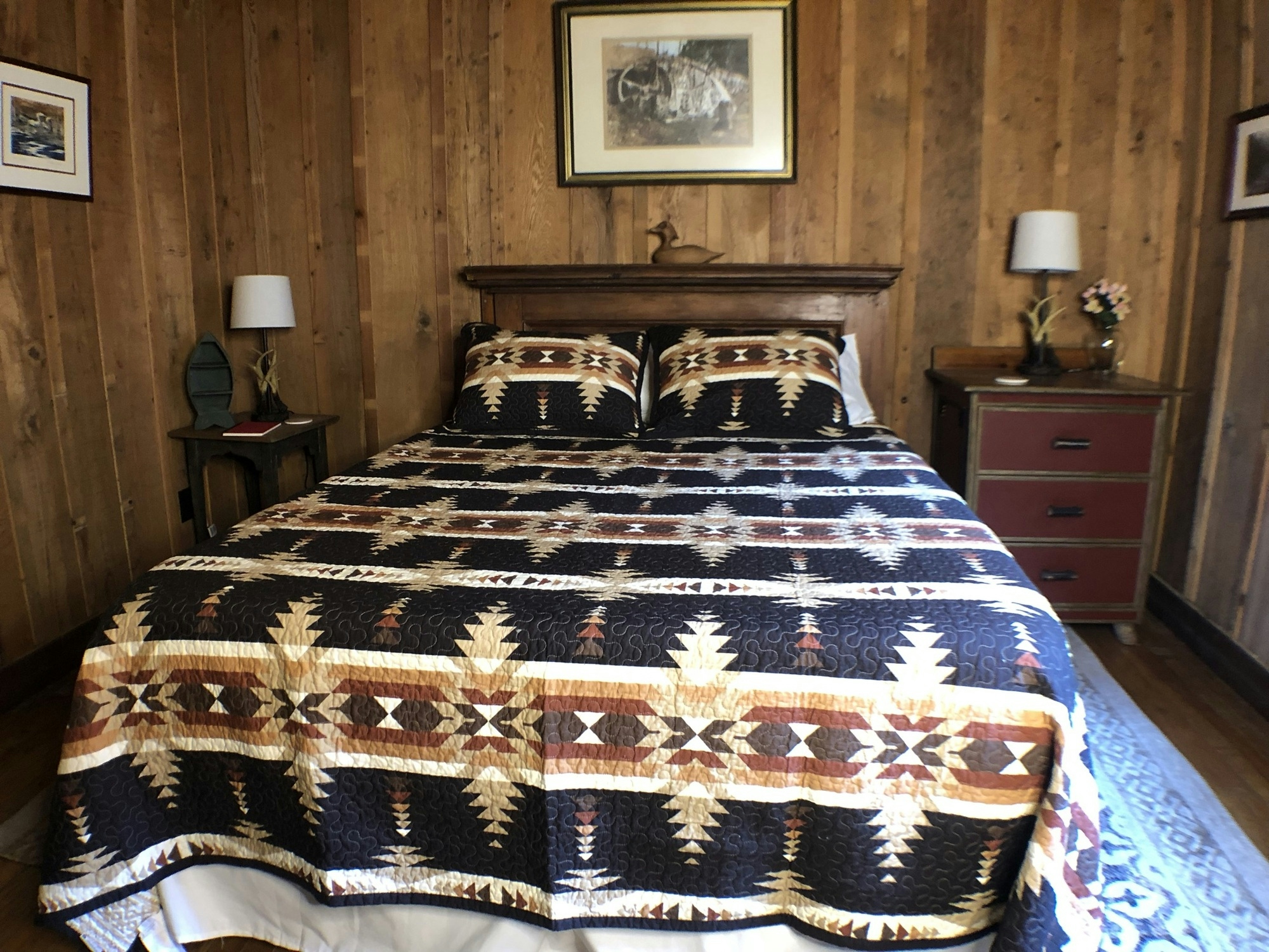 Rustic bedroom with a patterned bedspread, wooden headboard, and wooden walls.