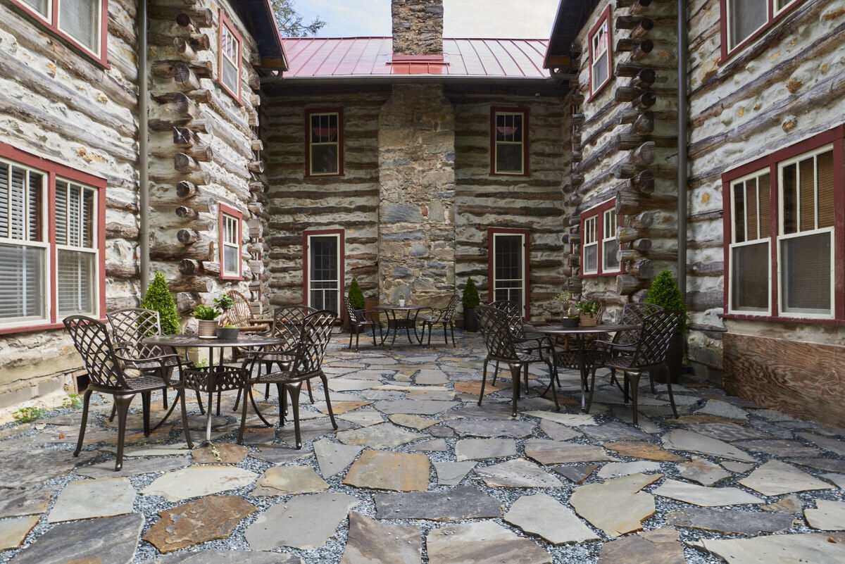 Stone patio with outdoor furniture surrounded by rustic log buildings.