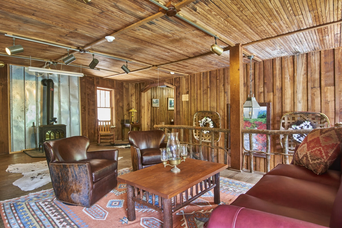 Spacious rustic living room with wooden walls, leather chairs, a red sofa, and a wood-burning stove.