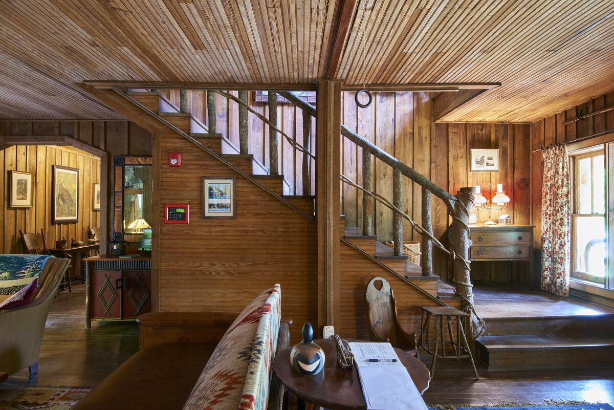 Rustic living area with wooden walls, a staircase, and a cozy seating area.