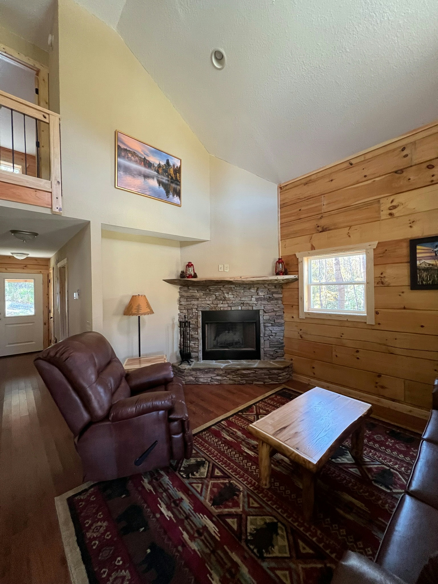 Cozy living room with high ceilings, a stone fireplace, leather recliners, and a wooden coffee table.