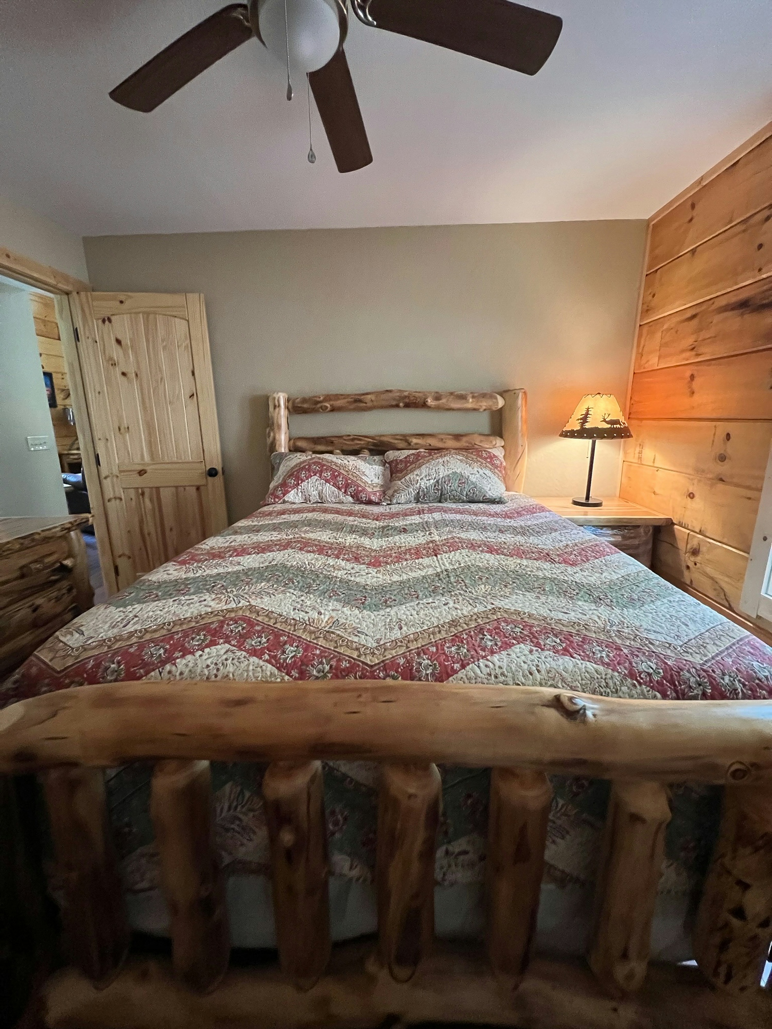 Rustic bedroom with a wooden bed frame, patterned quilt, and ceiling fan.