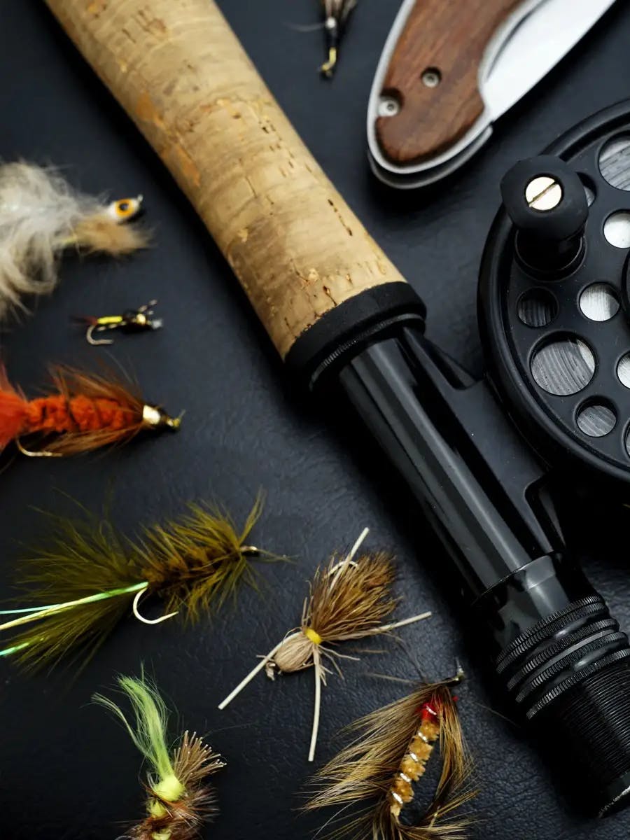 Close-up of fly fishing equipment, including a rod, reel, knife, and various fishing flies.