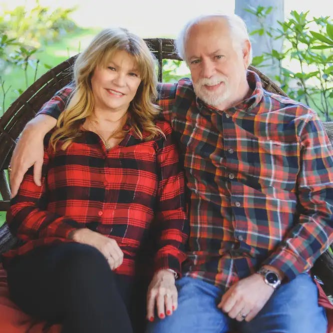 Older couple wearing matching plaid shirts, sitting close together and smiling on a porch swing.