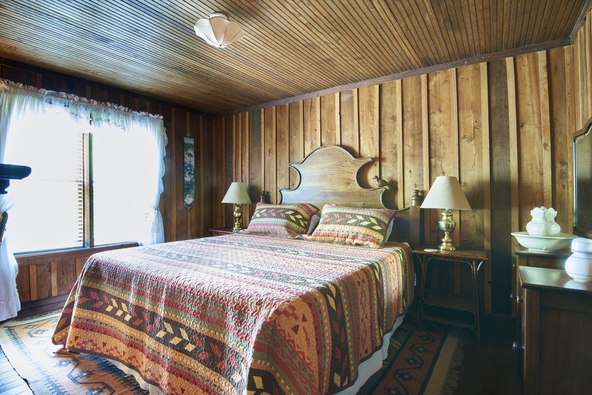 Rustic bedroom with a wooden headboard, colorful patterned bedspread, and wooden walls.