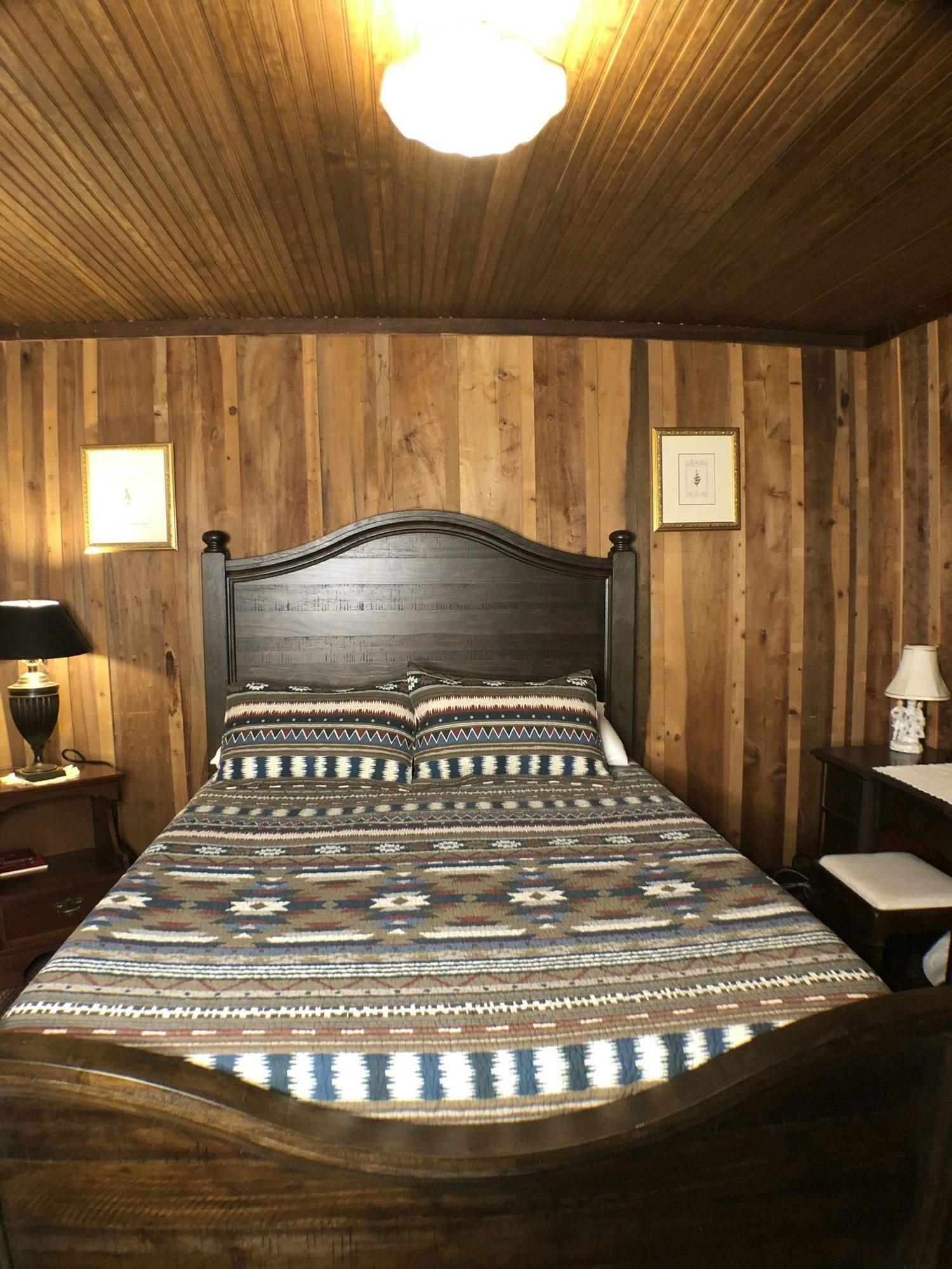 Rustic bedroom with a dark wooden bed frame, patterned bedspread, and wooden walls.