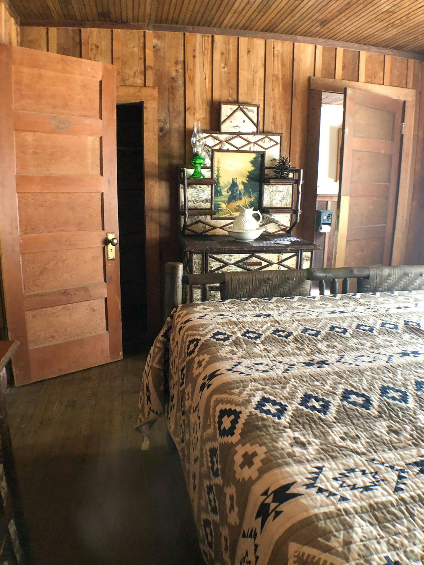 Rustic bedroom with a patterned bedspread, wooden doors, and a dresser with decorative items.