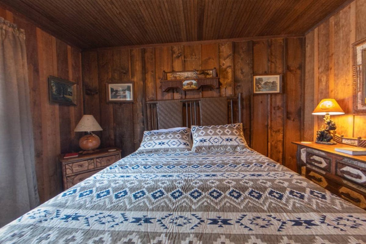 Rustic bedroom with a wooden headboard, patterned bedspread, and warm lighting.