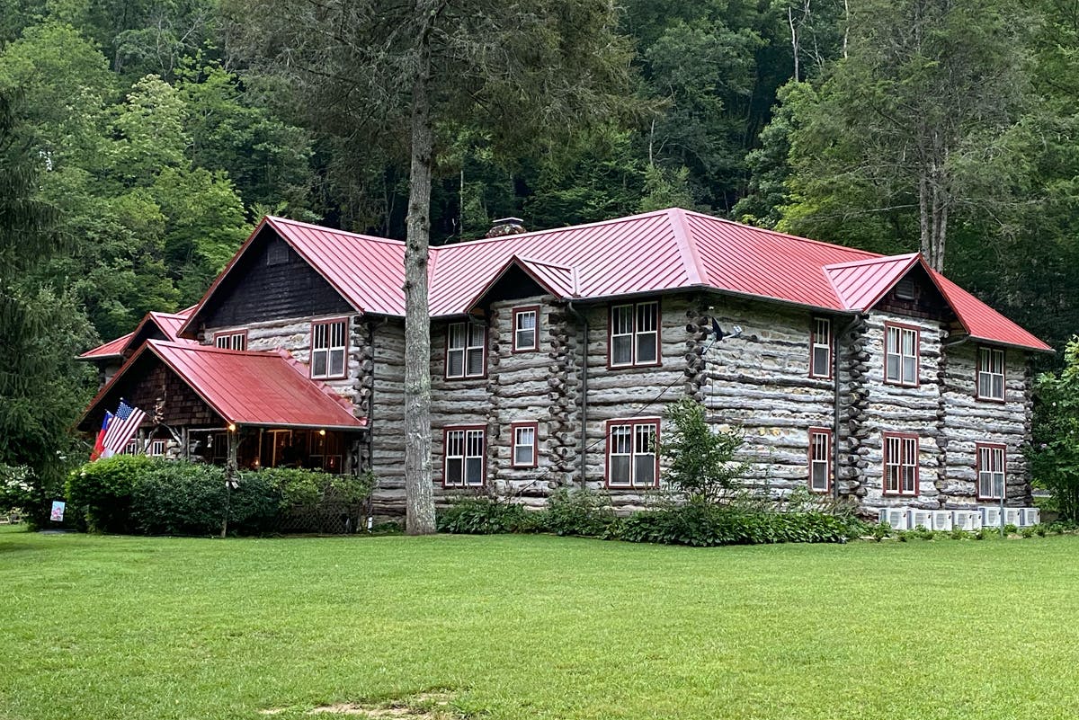 Rustic log house with a red roof surrounded by greenery and trees.