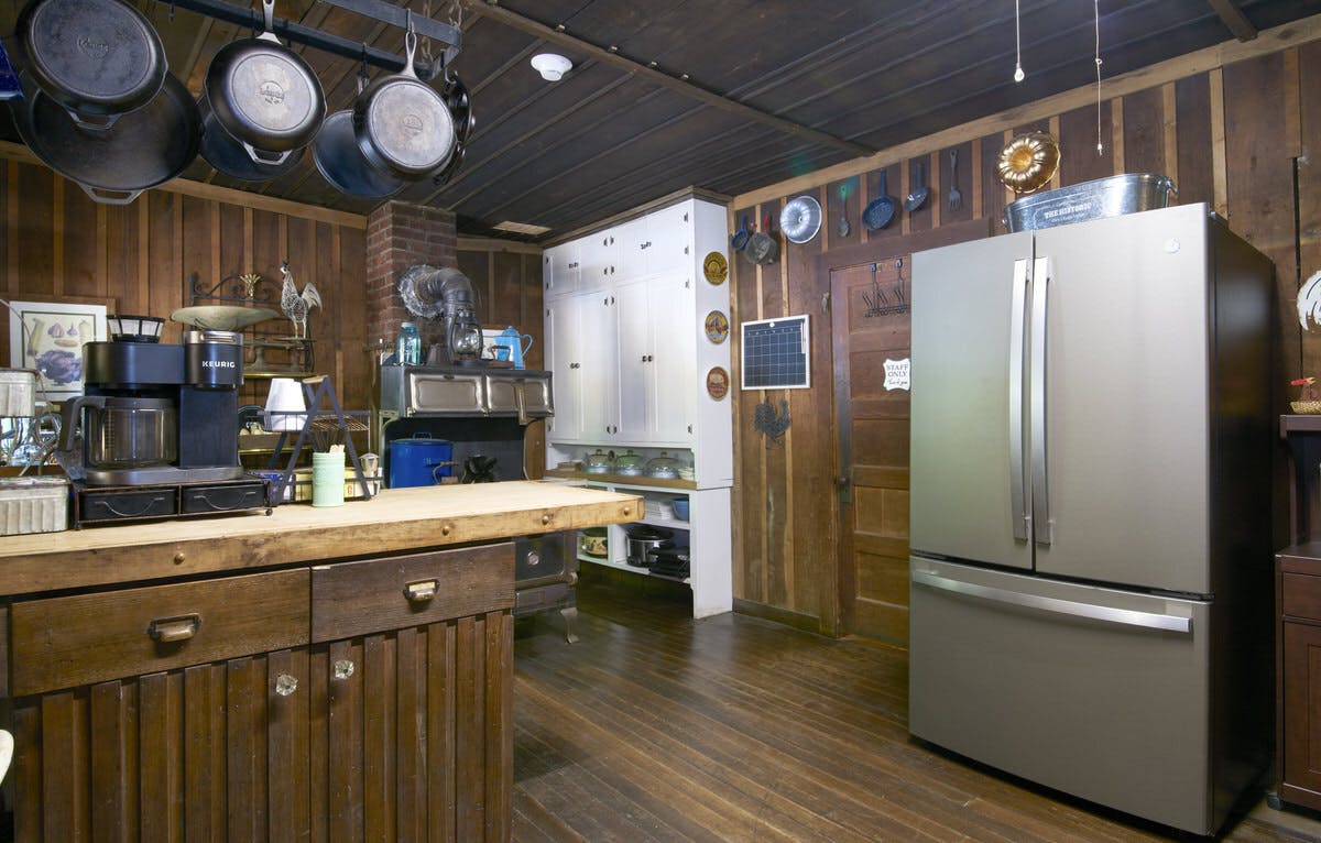 Rustic kitchen with wooden cabinets, a stainless steel refrigerator, and hanging pots and pans.