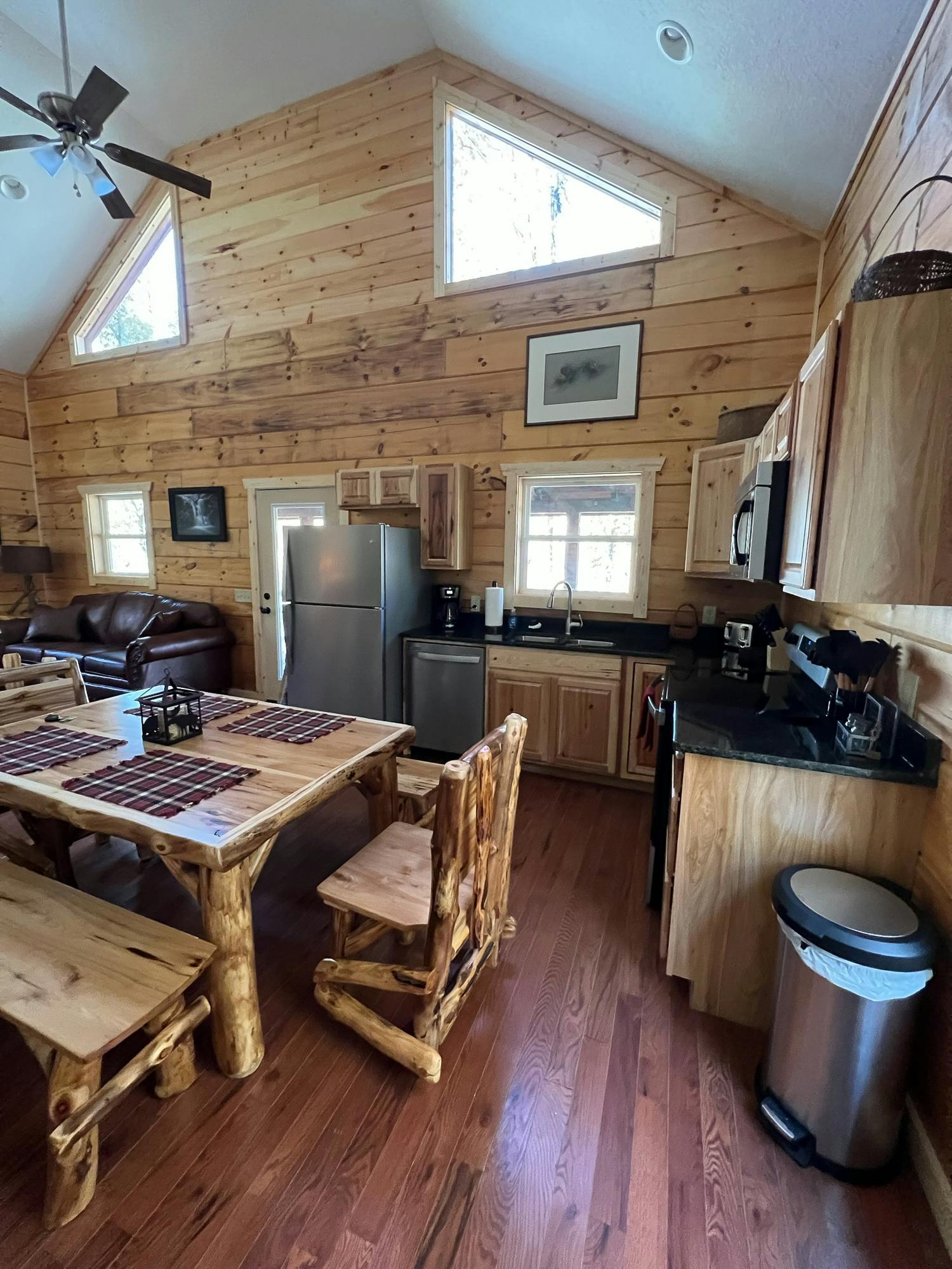 Open-concept kitchen and dining area with wooden furniture, high ceilings, and stainless steel appliances.